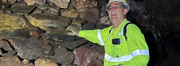 Kyle Ehnes  underground at SURF wearing a reflective shirt and proper PPE smiling with his had on a rock wall. 