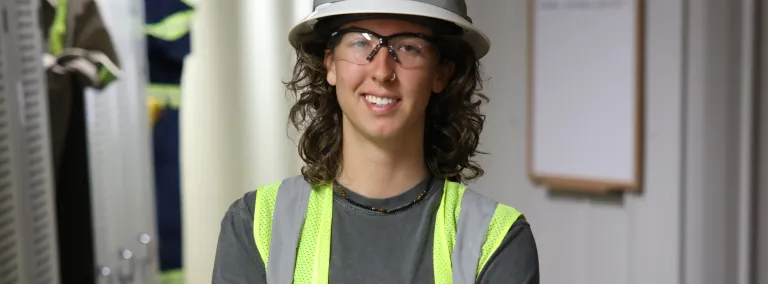 Raine Flick, a 2024 summer intern at SURF, poses in a hardhat, safety glasses and a reflective vest in near the Yates dry SURF.