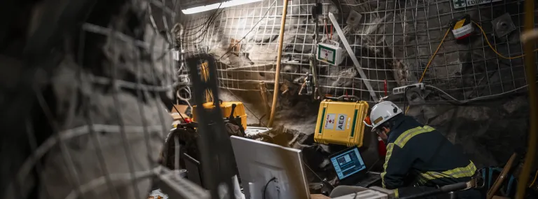 A researcher sits in a drift, looking at a computer. The drift is heavily outfitted with scientific monitoring equipment.