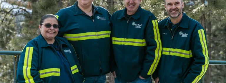 Four people in reflective gear stand in front of trees