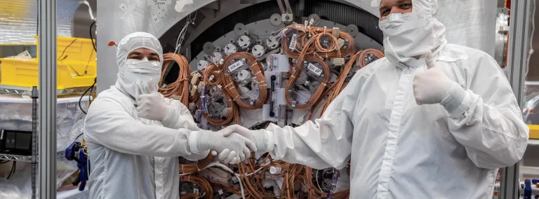 Two people in Tyvek suits shaking hands with thumbs up