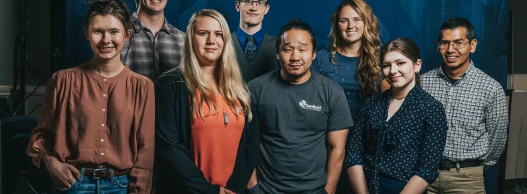 Eight people smile at the camera in front of a blue backdrop