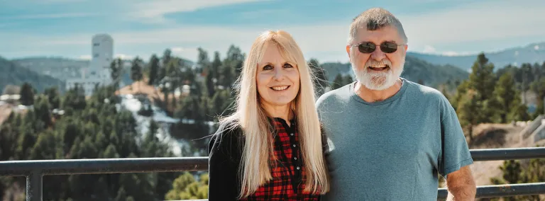 Eileen Brosnahan (left) and Martin Brosnahan (right) stand in front of Kirk Canyon with the Ross Headframe in the distance.