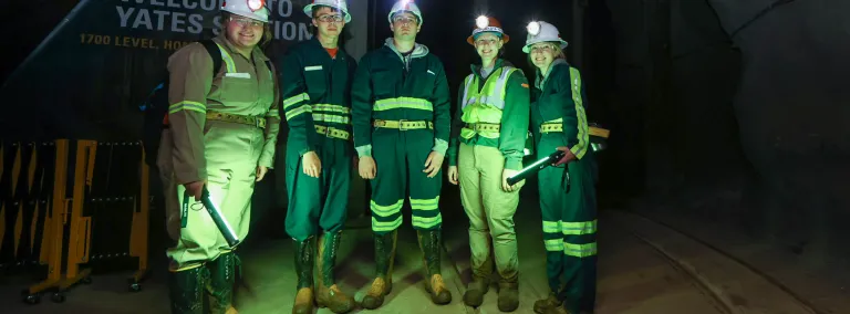 SURF's 2022 summer interns stand in front of the Yates Shaft station, illuminated by green, portable lights 