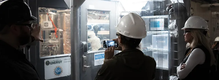 a visitor takes a photo of researchers working inside a cleanroom