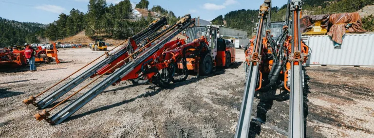 two jumbo drill rigs in a parking lot