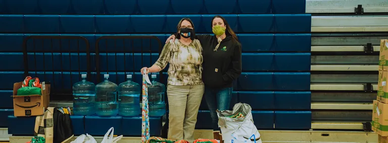 Two people wearing masks stand together in front of holiday gifts for students