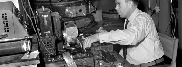 Man in glasses sits in front of a table of scientific apparatus