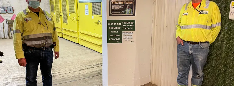 Two workers in masks and high visibility shirts stand on either side of the Stratton Station plaque.