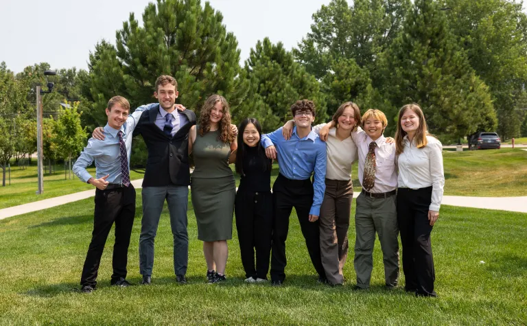 The 2024 Davis-Bahcall Scholars include: (L-R) Colby Routh, Beck Bruch, Nicolette Dame, Huixin Zhang, James Roth, Mackenzie Hollenbeck, Jing Yan, and  Ashley Tieszen - standing on green grass outside dressed up for their presentations.  