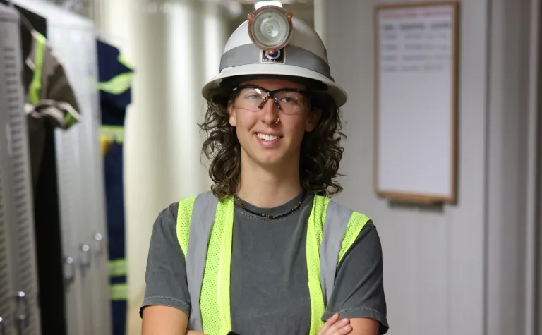 Raine Flick, a 2024 summer intern at SURF, poses in a hardhat, safety glasses and a reflective vest in near the Yates dry SURF.