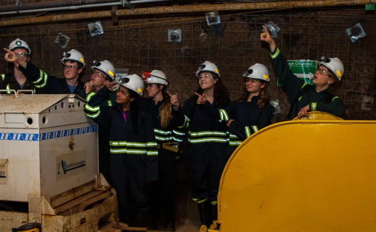 students stand underground pointing into the middle distance