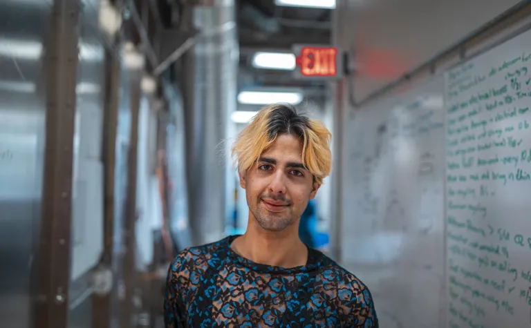 Researcher stands in a hallway with windows and whiteboard behind him