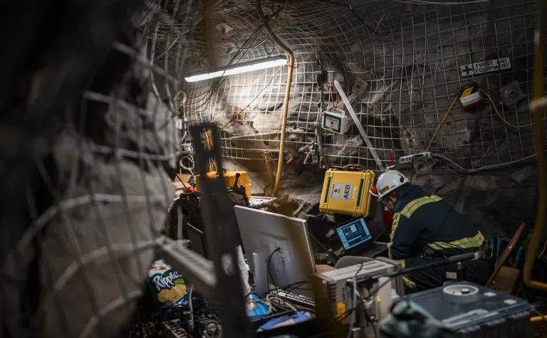 A researcher sits in a drift, looking at a computer. The drift is heavily outfitted with scientific monitoring equipment.