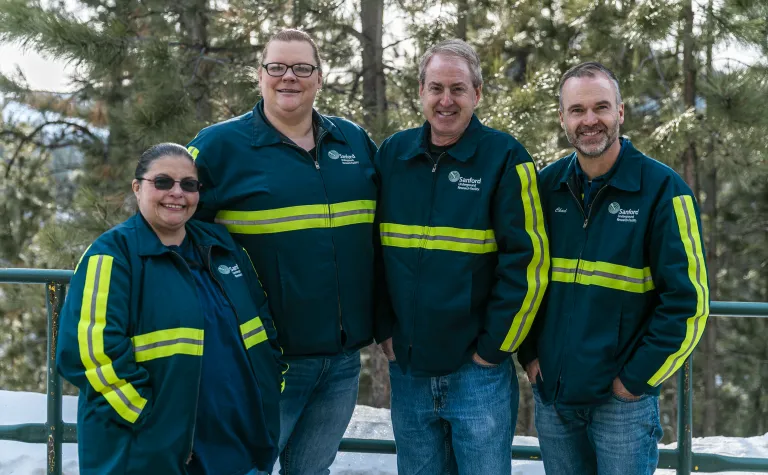 Four people in reflective gear stand in front of trees