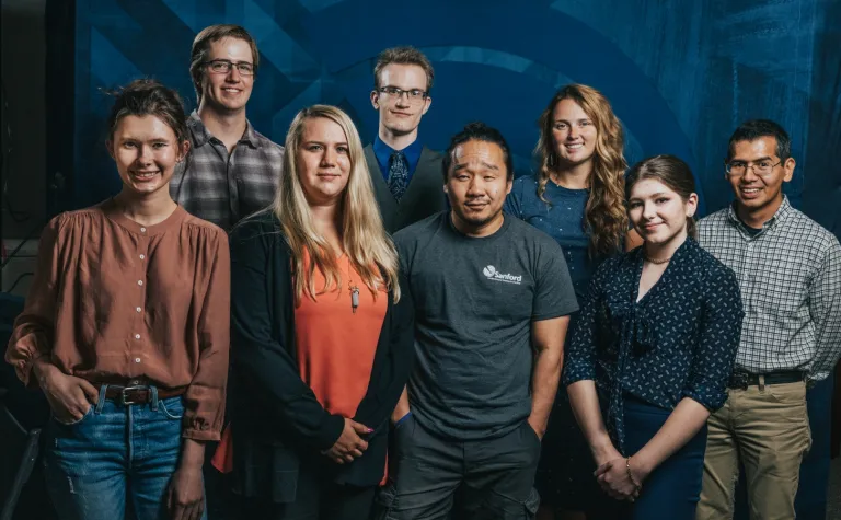 Eight people smile at the camera in front of a blue backdrop