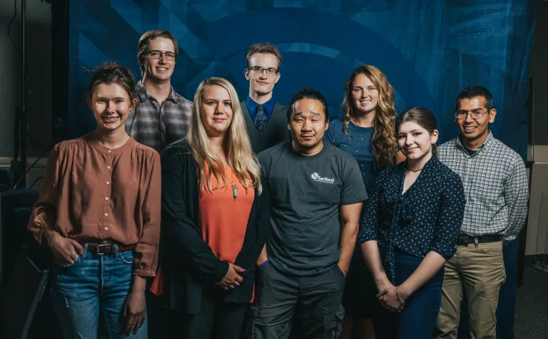 Eight people smile at the camera in front of a blue backdrop