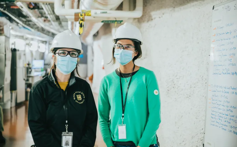 two masked people stand in an underground hallway