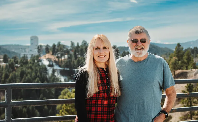 Eileen Brosnahan (left) and Martin Brosnahan (right) stand in front of Kirk Canyon with the Ross Headframe in the distance.