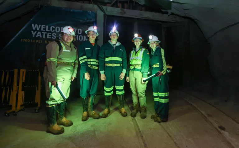 SURF's 2022 summer interns stand in front of the Yates Shaft station, illuminated by green, portable lights 