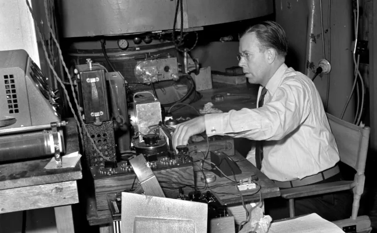 Man in glasses sits in front of a table of scientific apparatus