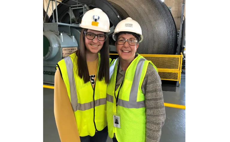 Two people in hardhats stand in the hoistroom.