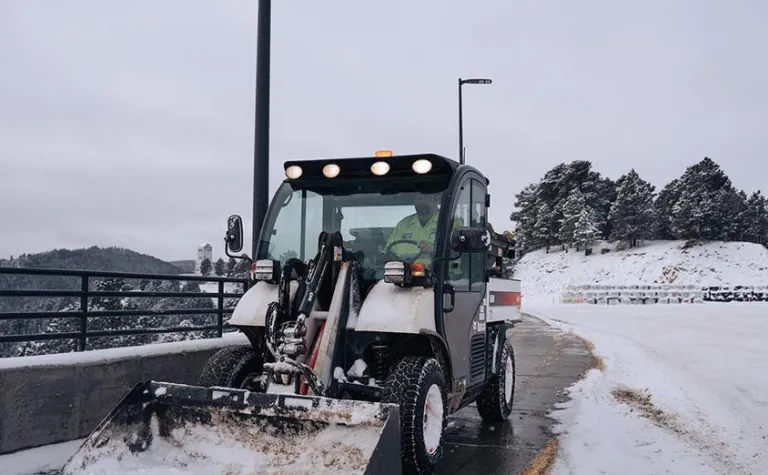 Worker operates a bobcat to remove snow from the parking lot