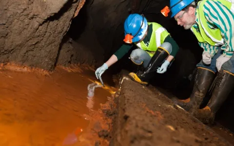 people collecting water sampels from a trough of red + rusty looking water in a drift underground at SURF.  