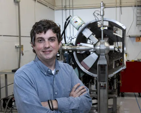 ORNL’s Mitch Allmond stands in a lab before a large radiation detector, developing models and experiments on atomic nuclei.