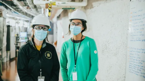 two masked people stand in an underground hallway