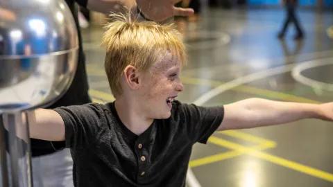 A child takes part a science learning activity utilizing a Van De Graaff generator brought to Neutrino Day 2024 by South Dakota Mines. 